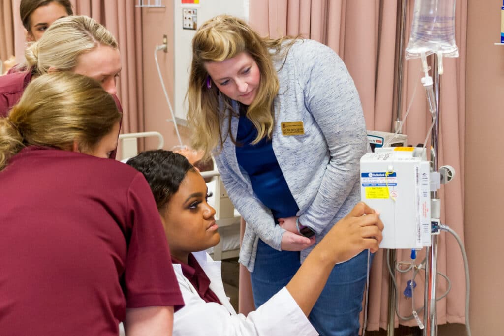ADN student adjusts an IV Infusion Pump while instructor and other students observe at PRCC.