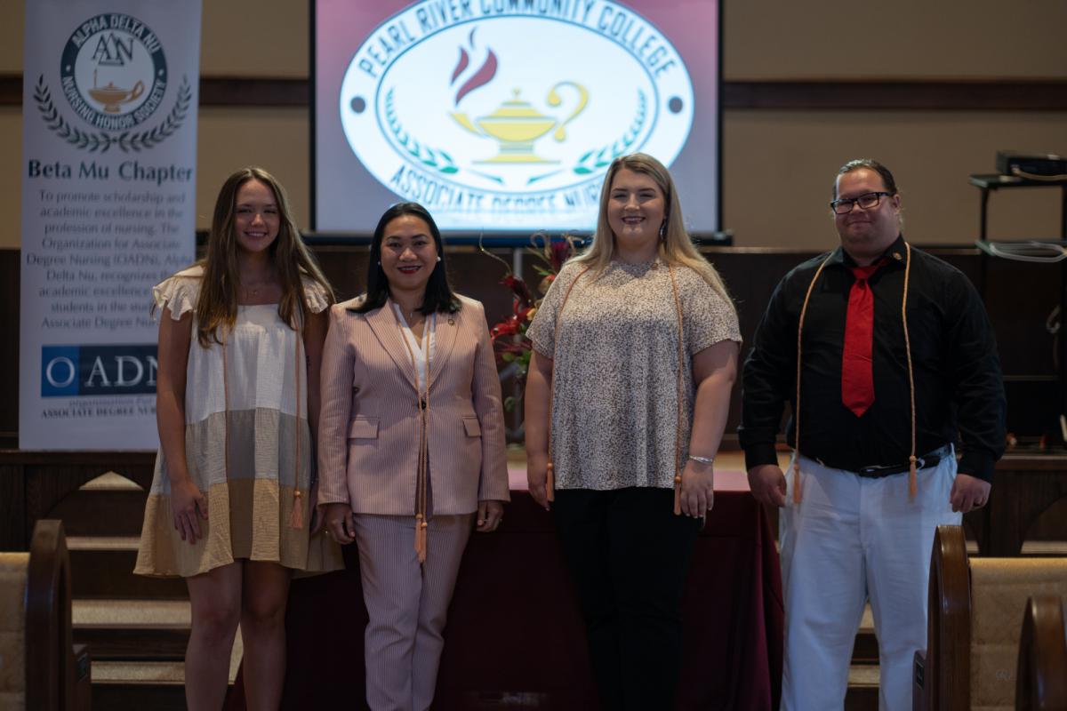 Four nursing students stand in front of banner for Alpha Delta Nu Nursing Honor Society