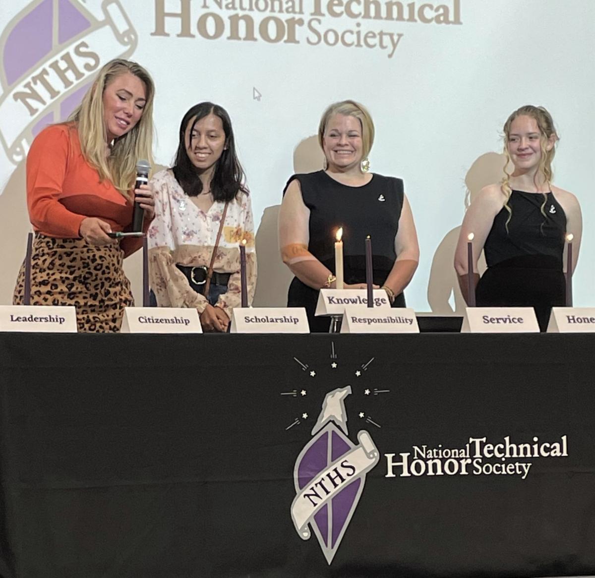 Woman lights candle while three other women look on at the National Technical Honor Society induction March 2022