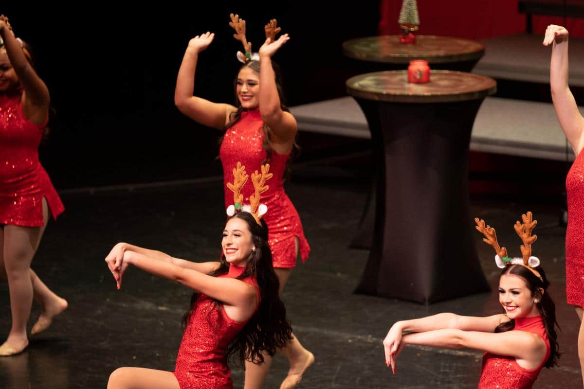 Girls wearing red costumes and reindeer headbands dance on stage
