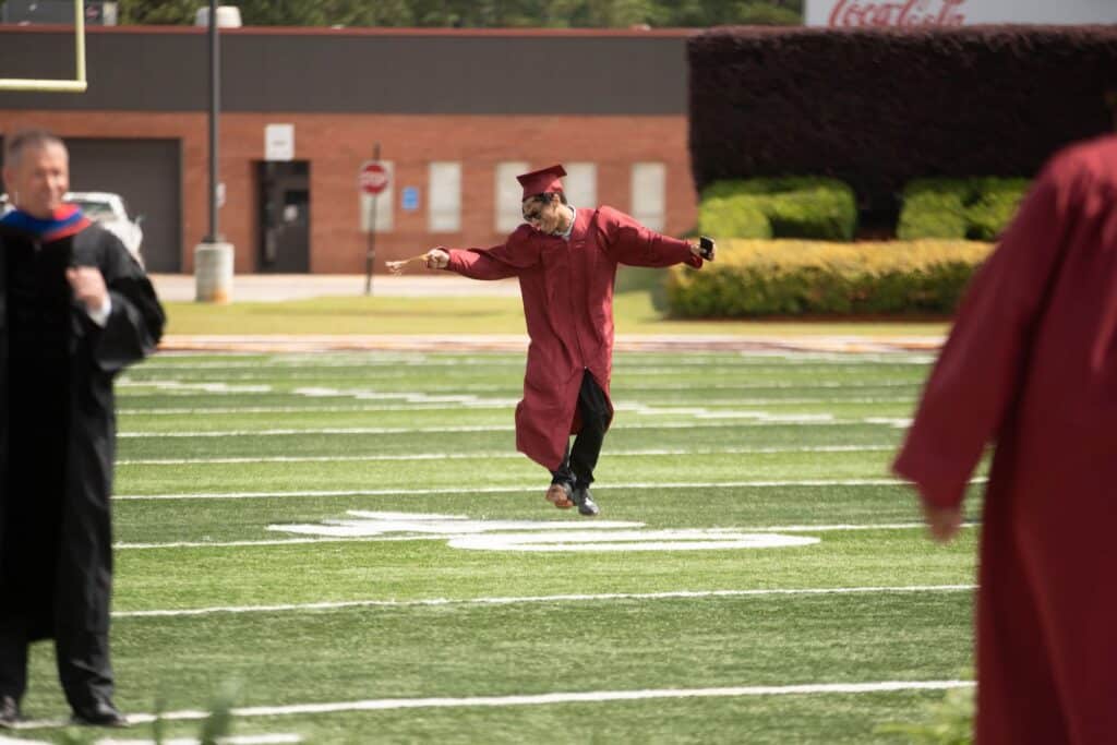 Young man wearing maroon robes dances at graduation.