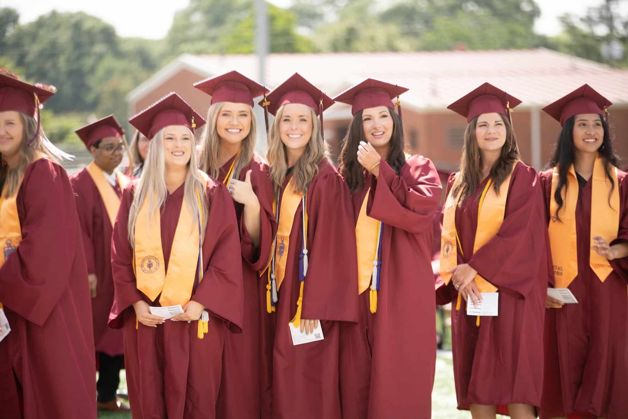 Group of young women wearing maroon robes wait in line at graduation.