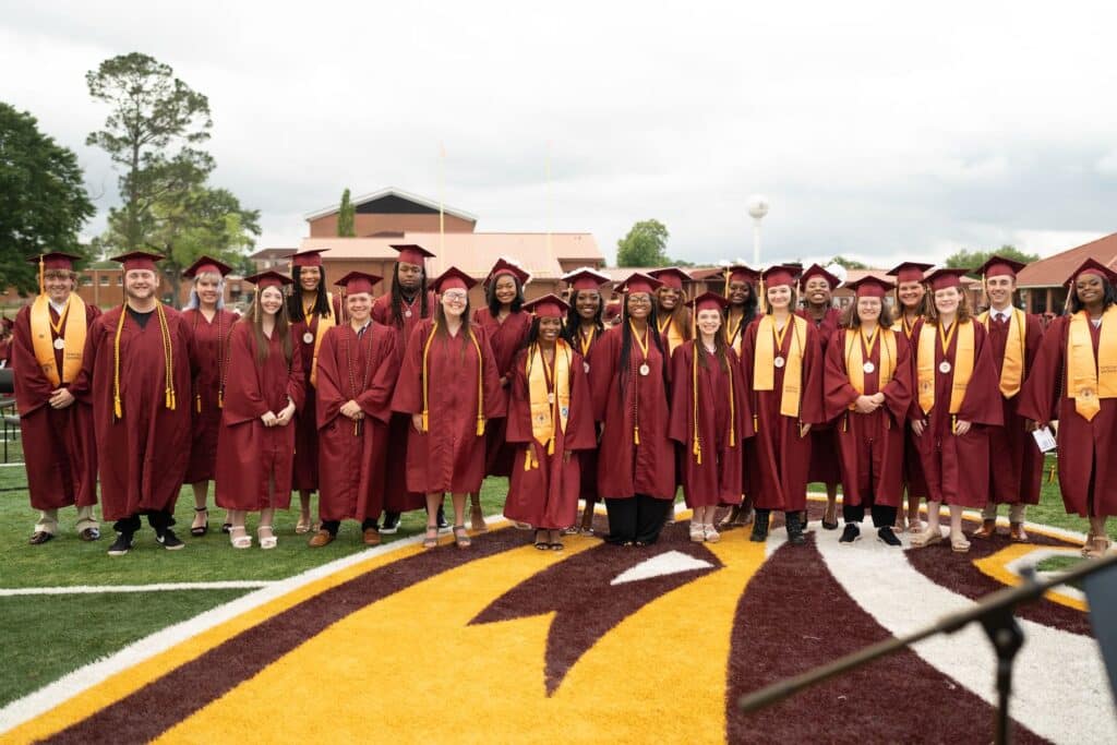 Group of high school students wearing maroon robes on football field.