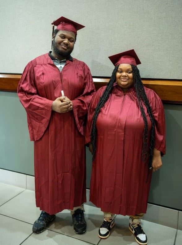 Man and woman stand together while wearing graduation cap and gown.
