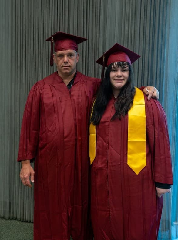 Father and daughter in maroon caps and gowns.