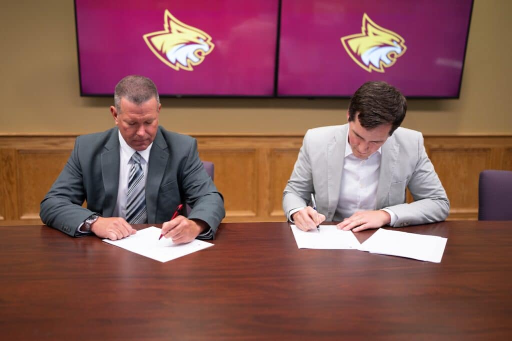 Two men sign papers at conference table.