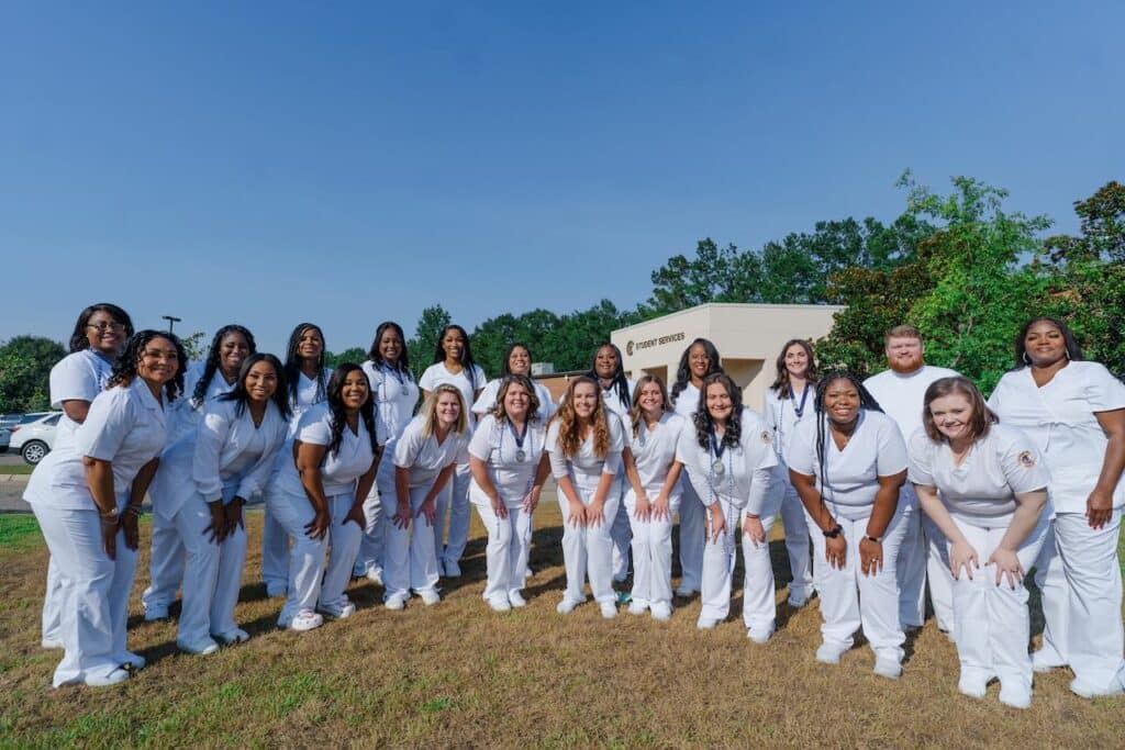 Twenty Two people wearing white scrubs stand in 2 lines outside.