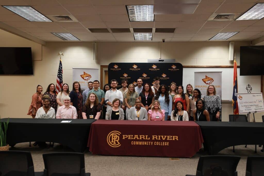 Dozens of nursing students sit and stand behind tables with Pearl River Community College on the tablecloth.