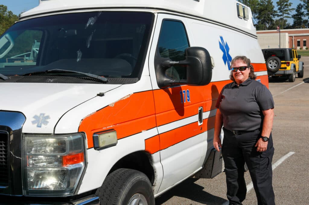 Woman stands next to ambulance in parking lot.