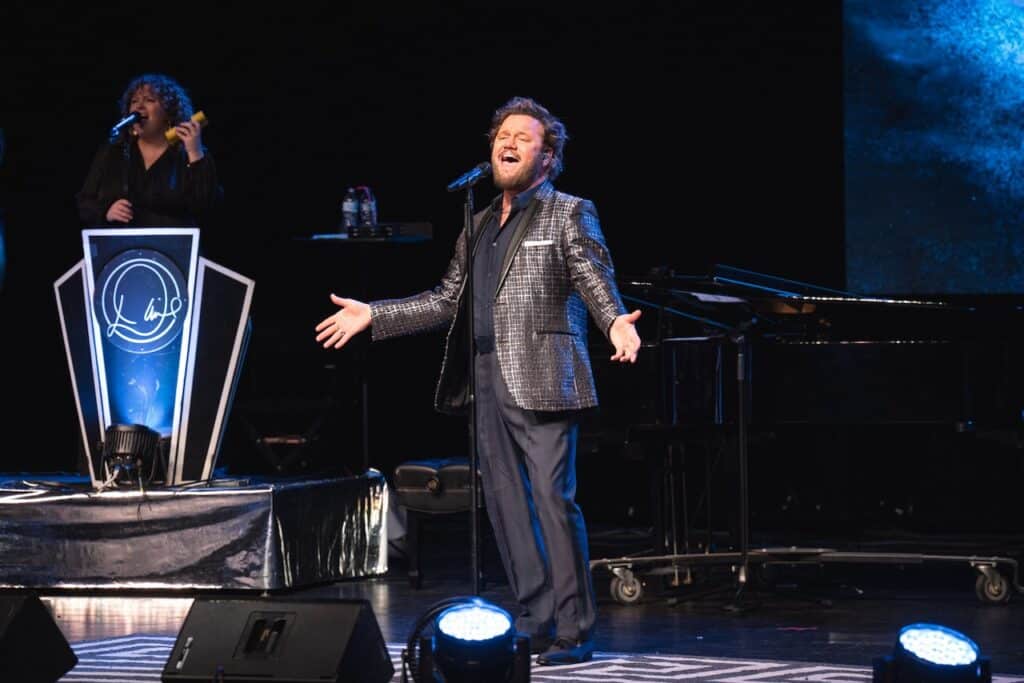 David Phelps sings on stage with piano behind him and daughter Callie singing off to the left.