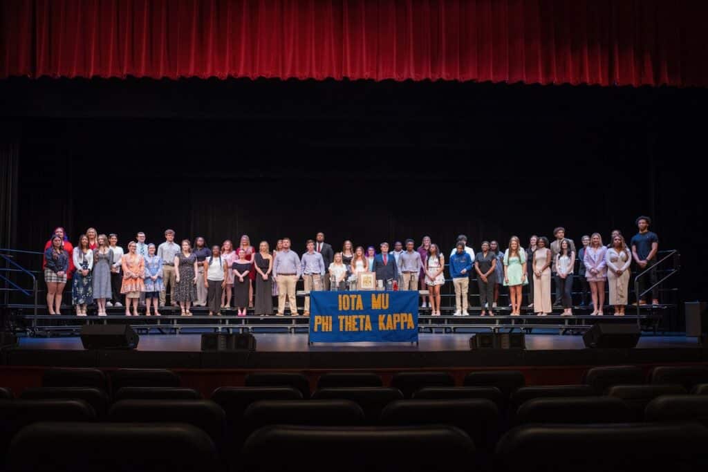 46 men and women stand on stage in two long rows.