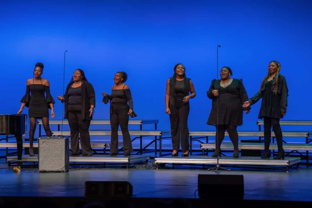 Six women in black perform on stage.