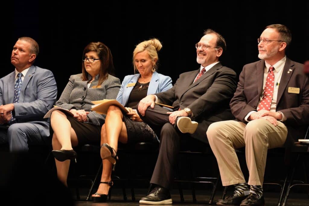 Three men and two women sit in a row on stage.
