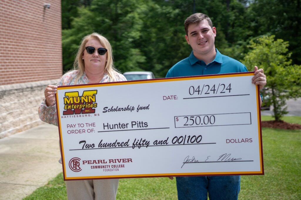 Woman wearing sunglasses and young man hold oversized check with trees in background.
