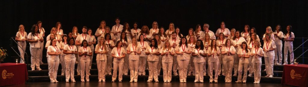 Students wearing white scrubs while holding lit lamps.