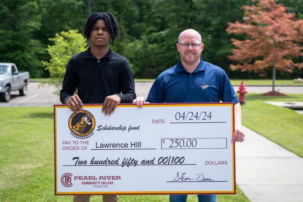 Two men hold oversized check. Trees and grass in background.