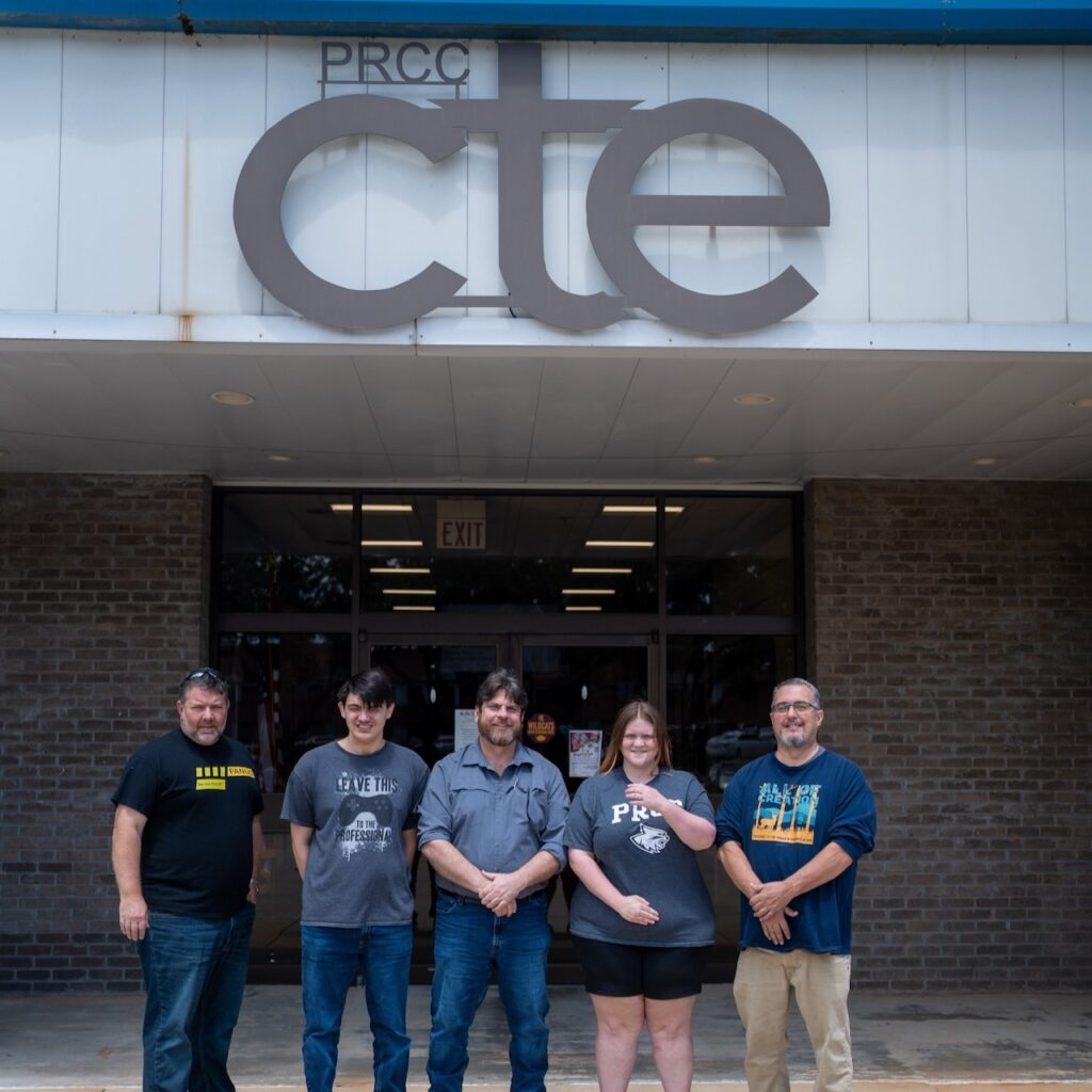 Four men and one woman stand outside building with PRCC CTE above them.